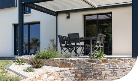 Carport pergola bioclimatique intégrant un espace détente, bordé par un massif de plantes et de graviers